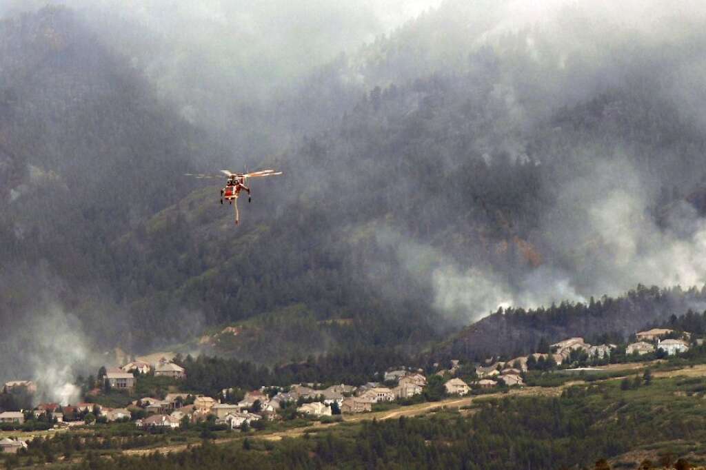 A helicopter flies over as the Waldo Canyon Fire continues to burn Wednesday, June 27, 2012, in Colorado Springs, Colo. The wildfire doubled in size overnight to about 24 square miles (62 square kilometers), and has so far forced mandatory evacuations for more than 32,000 residents.(AP Photo/Bryan Oller)