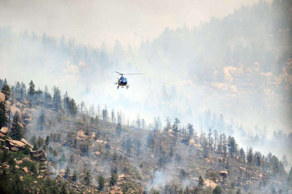 A helicopter flies over a wildfire burning west of Manitou Springs, Colo., on Sunday, June 24, 2012. The fire erupted and grew out of control to more than 3 square miles early Sunday, prompting the evacuation of more than 11,000 residents and an unknown number of tourists. (AP Photo/The Colorado Springs Gazette, Christian Murdock)