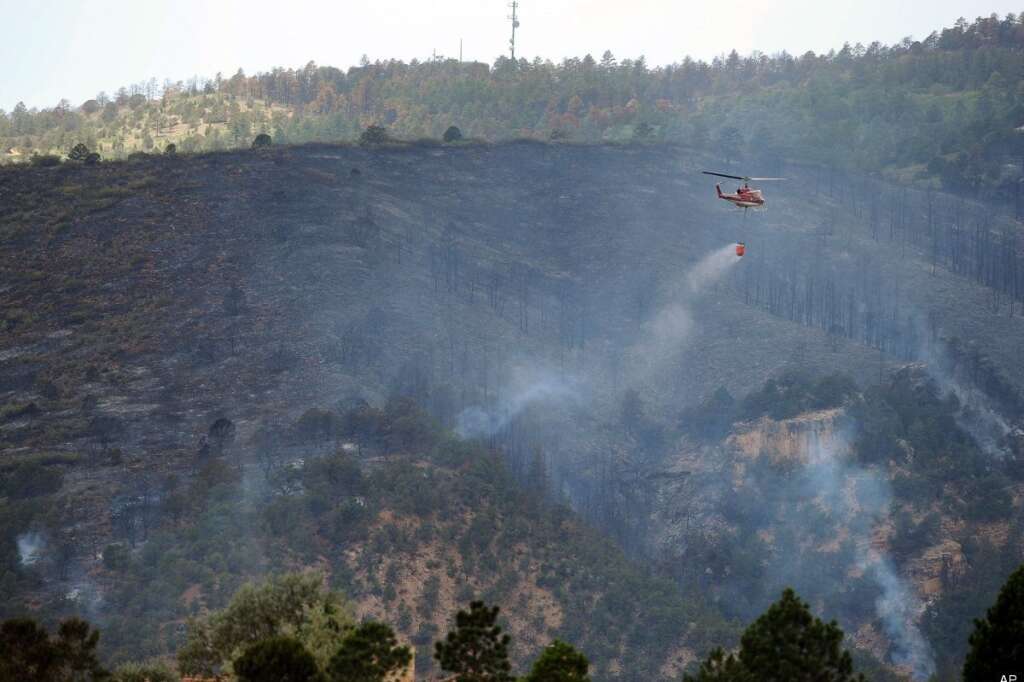 A helicopter drops water as the Waldo Canyon Fire burns Wednesday, June 27, 2012, in Colorado Springs, Colo. The wildfire doubled in size overnight to about 24 square miles (62 square kilometers), and has so far forced mandatory evacuations for more than 32,000 residents. (AP Photo/The Gazette, Christian Murdock)