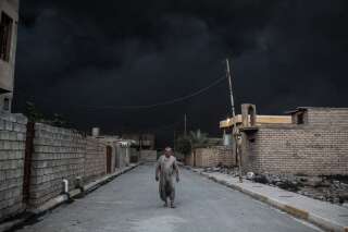 Un homme marche dans une rue de Mossoul. Derrière lui, un épais nuage de fumée provoqué par l'incendie d'un puits de pétrole