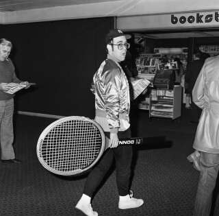 Elton John pictured at Heathrow Airport, arriving back from America, carrying a huge tennis racket, 8th April 1978. (Photo by Peter Stone/Mirrorpix/Getty Images)