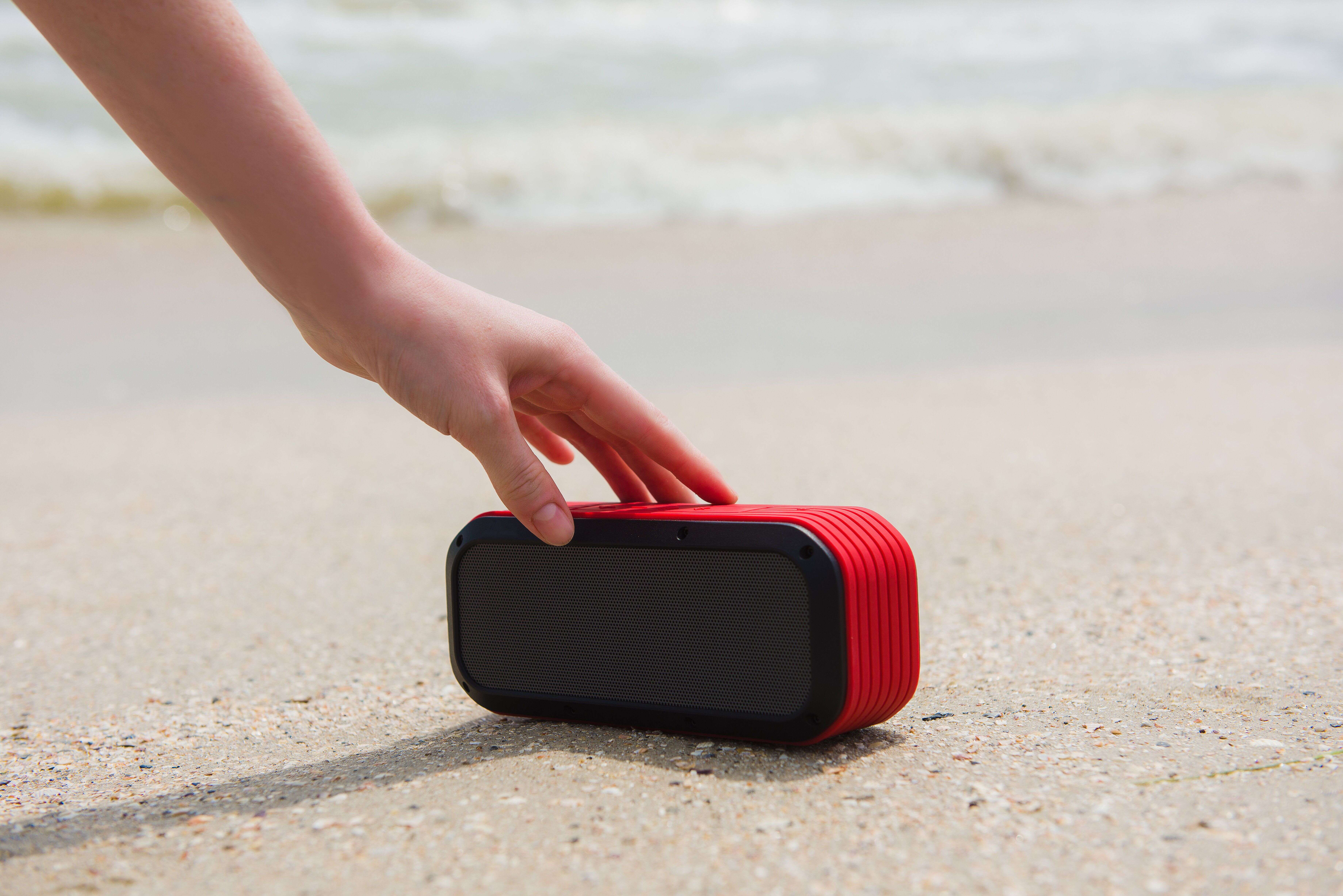 Female hand touch portable speaker. Woman and usb wireless acoustic at beach with sand