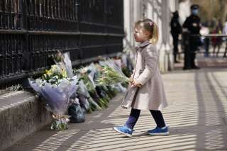 Une fillette dépose des fleurs devant les grilles du Buckingham Palace à Londres le 9 avril 2021 après l'annonce de la mort du prince Philip.