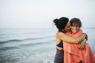Portrait of a smiling mature woman and her twelve years old boy, embracing and kissing on the beach during sunset