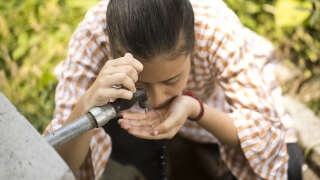 Thirsty teenage girl drinking tap water outdoors in field