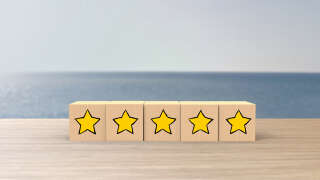 Wooden cartoon cube five yellow star review on blur sea with the sky background. Service rating, satisfaction concept. reviews and comments google maps, tripadvisor, facebook. online evaluations.