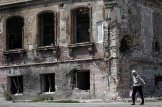 An elderly woman walks past a destroyed building in the city of Mariupol on August 1, 2022, amid the ongoing Russian military action in Ukraine. (Photo by STRINGER / AFP)