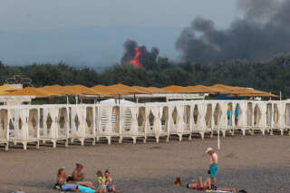People rest on a beach as smoke and flames rise after explosions at a Russian military airbase, in Novofedorivka, Crimea August 9, 2022. REUTERS/Stringer     TPX IMAGES OF THE DAY
