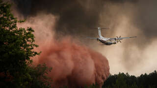A firefighting aircraft sprays fire retardant over trees during a wildfire near Saint-Magne, southwestern France, on August 11, 2022. (Photo by Philippe LOPEZ / AFP)