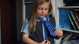 Little girl getting ready to go school trying to tie her school tie