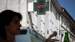 A woman has a drink with in background a pharmacy thermometer showing 42°C in Aigre, Charente, western France on June 17, 2022. - French officials have urged caution as a record pre-summer heatwave spread across the country from Spain, where authorities were fighting forest fires on a sixth day of sweltering temperatures. The Meteo France weather service said it was the earliest hot spell ever to hit the country, worsening a drought caused by an unusually dry winter and spring, and raising the risk of wildfires. (Photo by YOHAN BONNET / AFP)