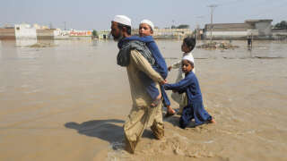 Un homme marche avec ses enfants au milieu des eaux le long d’une route à Nowshera, au Pakistan, après les inondations meurtrières.