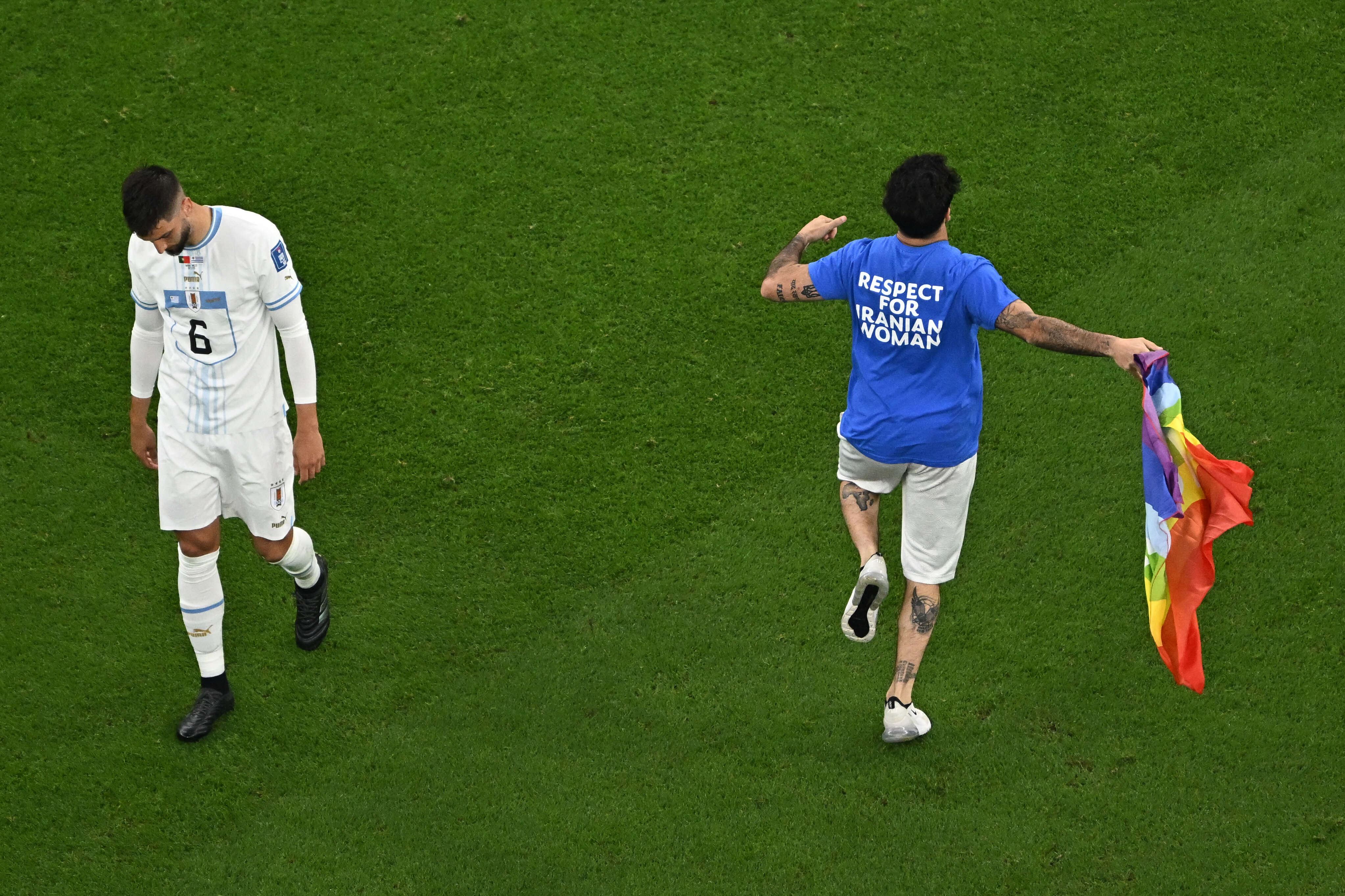 A man (R) invades the pitch holding a LGBT flag as he wears a t-shirt reading 