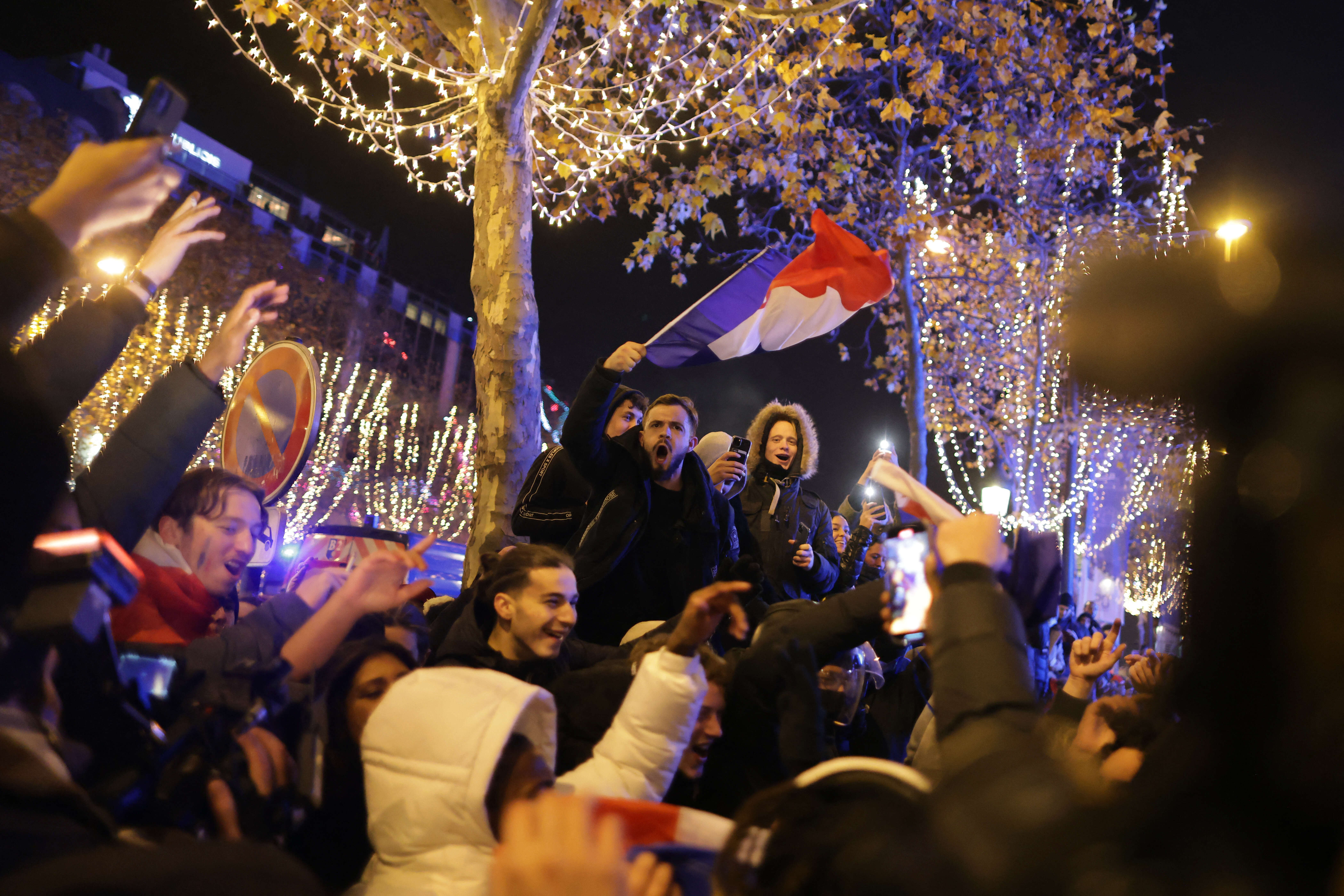 A football fan holds the French flag as he celebrates after France's victory over Morocco in the Qatar 2022 World Cup semi-final, on the Champs-Elysees in Paris on December 14, 2022. (Photo by Thibaud MORITZ / AFP)