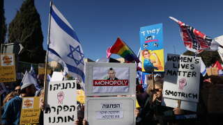 Des militants israéliens brandissent des drapeaux et des pancartes alors qu’ils manifestent devant la Knesset (parlement israélien) à Jérusalem, le 29 décembre 2022, contre l’assermentation du gouvernement de droite.