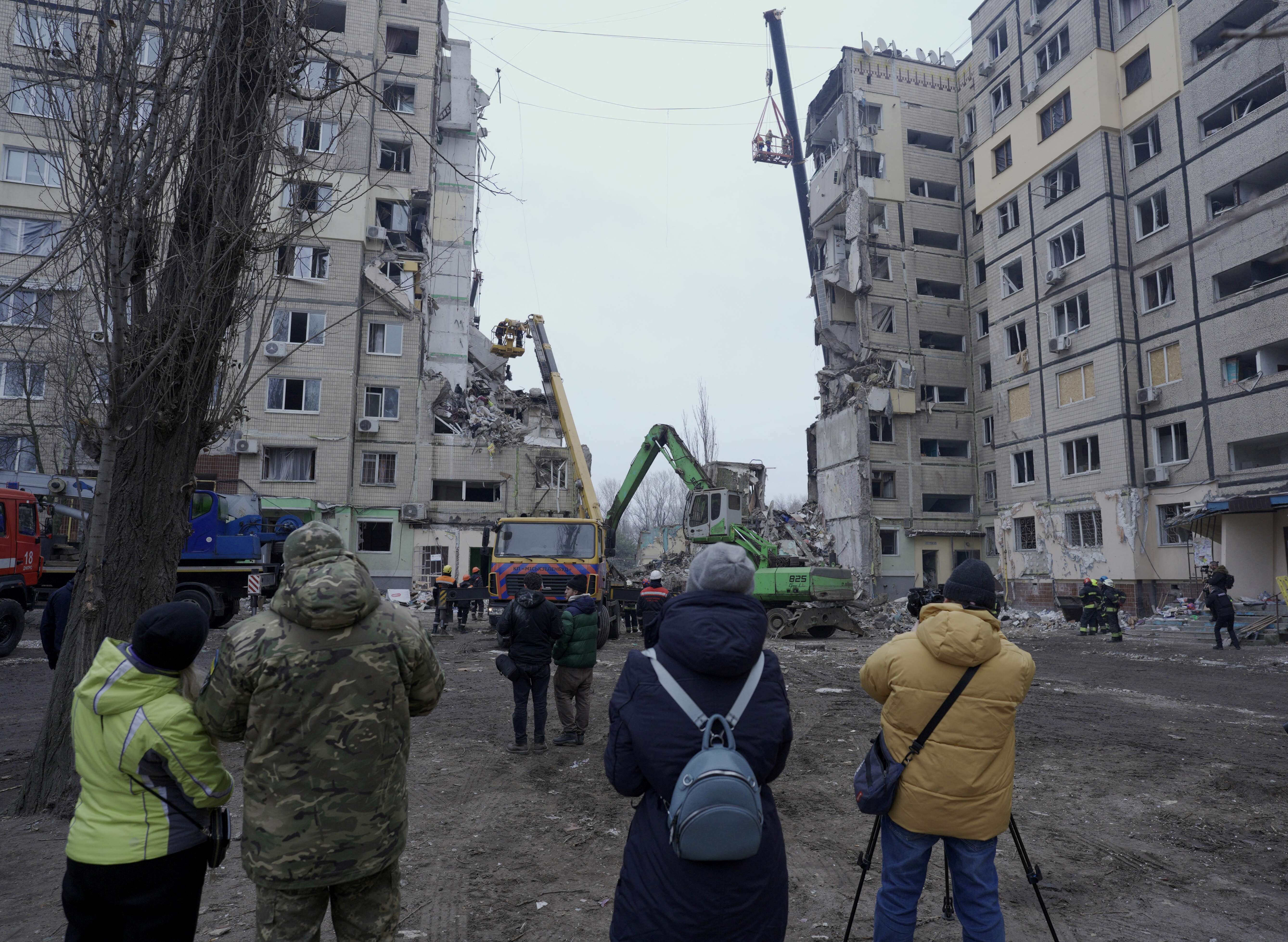 Local residents look at rescuers working on a residential building destroyed after a missile strike, in Dnipro on January 16, 2023, amid the Russian invasion of Ukraine. - According to State Emergency Service report, as of 1:00 pm on December 16, 40 people died, including 6 children; 75 people got injured, including 14 children; 39 people were rescued, including 6 children; the fate of 34 people is still unknown. (Photo by vitalii matokha / AFP)
