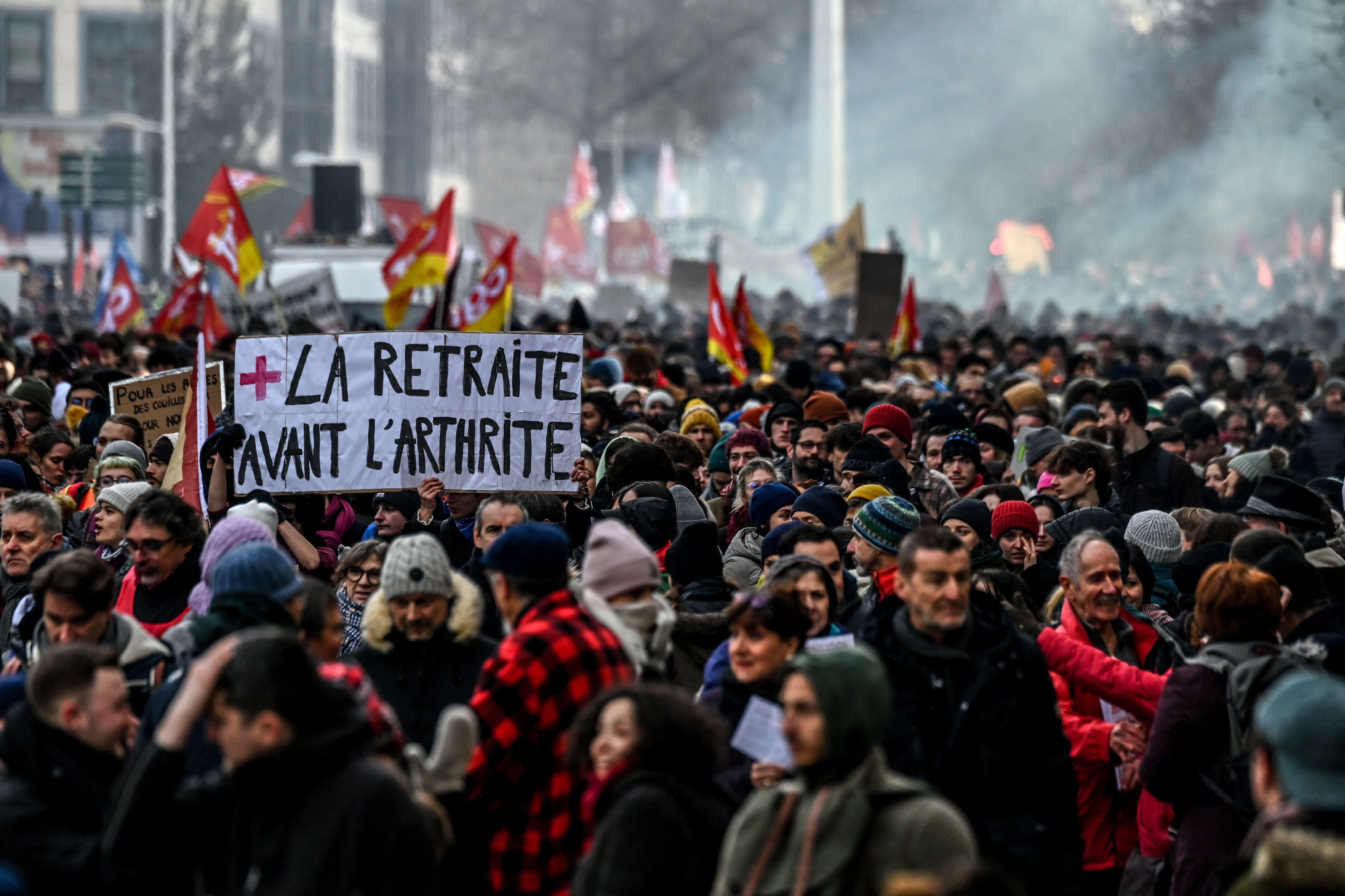 A protestor holds a placard which reads as 'retirement before arthritis' during a rally in Lyon, south-eastern France on January 19, 2023, as workers go on strike over the French President's plan to raise the legal retirement age from 62 to 64. - A day of strikes and protests kicked off in France on January 19, set to disrupt transport and schooling across the country in a trial for the government as workers oppose a deeply unpopular pensions overhaul. (Photo by OLIVIER CHASSIGNOLE / AFP)