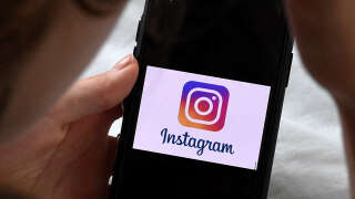 In this photo illustration, a person looks at a smart phone with a Instagram logo displayed on the screen, on August 17, 2021, in Arlington, Virginia. (Photo by OLIVIER DOULIERY / AFP)