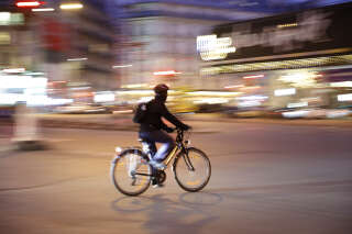 A warm color, night-time panning image of a cyclist at an intersection in Paris with bright city lights in the background.