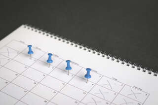 Blue pins on four days in a week on a calendar. Friday, Saturday and Sunday crossed out. Four day work week concept.