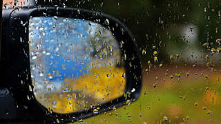 View  through the window of my car on the outside rear view mirror in which you can see bright colors reflected. On the window there were big raindrops. The rain was heavy and it was in December in South East of France , i was inside the car