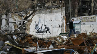 A local resident walks past a graffiti on a wall of destroyed building, drawn in Banksy style but its origin unconfirmed by the artist, in the town of Borodyanka on November 12, 2022, amid the Russian invasion of Ukraine. - Banksy, the elusive British street artist, has painted a mural on a bombed-out building outside Ukraine's capital, in what Ukrainians have hailed as a symbol of their country's invincibility. On November 11's night the world-famous graffiti artist posted on Instagram three images of the artwork -- a gymnast performing a handstand amid the ruins of a demolished building in the town of Borodyanka northwest of the Ukrainian capital Kyiv. (Photo by Genya SAVILOV / AFP) / RESTRICTED TO EDITORIAL USE - MANDATORY MENTION OF THE ARTIST UPON PUBLICATION - TO ILLUSTRATE THE EVENT AS SPECIFIED IN THE CAPTION