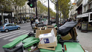 Pedestrians walk past unemptied garbage bins and plastic bags during a strike of garbage collectors in a street in Paris on October 8, 2015. Garbage collectors in the French capital have been on strike for the last three days, demanding the revaluation of their salaries. AFP PHOTO / ERIC FEFERBERG (Photo by ERIC FEFERBERG / AFP)
