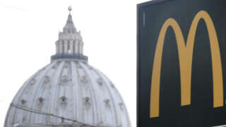 A sign showing the direction of a McDonald's restaurant is seen with the cupola of St Peter's basilica in the background, on January 3, 2017 in Rome. The US fast-food chain opened a restaurant in a Vatican-owned building despite protest of a Committee for the Protection of Borgo, the historic district around the Vatican where many cardinals live. (Photo by Tiziana FABI / AFP)
