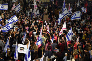 Des manifestants pro démocratie bloquent une route et brandissent des drapeaux nationaux lors d’un rassemblement contre la réforme judiciaire du gouvernement israélien à Tel Aviv, le 27 mars 2023, au lendemain du renvoi du ministre de la Défense israélien.