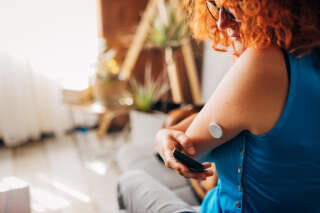 Mid-adult woman with chronic disease, and type 1 diabetes, using the reader device, an continuous glucose monitor, above the glucose blood sensor, to read her blood sugar level, so she can know when is time for insulin dose