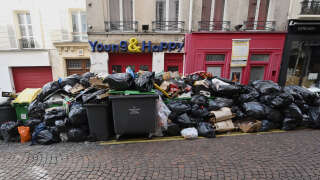 A restaurant worker throws waste atop a trash pile in Paris after waste collectors went on strike against pension reforms, leaving many streets in the capital piled with waste on March 20, 2023. - The amount of trash uncollected on Paris streets due to a waste workers strike has surged to 10,000 tonnes, despite efforts to force them back to duty, authorities said on March 17, 2023. (Photo by Emmanuel DUNAND / AFP)