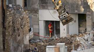 An firefighter looks on as an excavator moves rubble at 'rue Tivoli' a day after a building collapsed in the street, in Marseille, southern France, on April 10, 2023. - An apartment building collapsed in an apparent explosion on April 9, 2023 in the French Mediterranean city of Marseille, injuring five people, with authorities warning up to 10 victims could be under the burning rubble. (Photo by NICOLAS TUCAT / AFP)