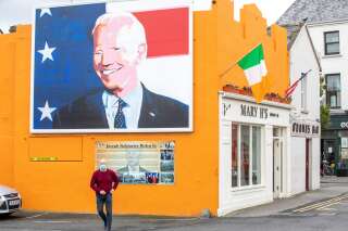 A pedestrian wearing a face mask or covering due to the COVID-19 pandemic, walks past a giant painting of US Presidential candidate Joe Biden, erected in his ancestral home of Ballina, north west Ireland, on October 7, 2020. - Thousands of miles east of the White House in Ireland, a pop-art portrait of US presidential candidate Joe Biden towers over his ancestral hometown of Ballina, County Mayo. In the town on Ireland's rugged Atlantic coast, the Democrat's distant relatives are thrilled to have one of their own bidding for America's highest office. 