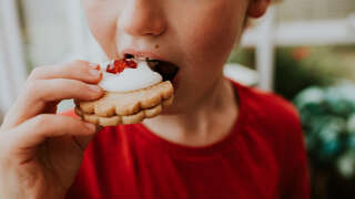 Young boy eating a double shortbread biscuit, topped with water icing and a glace cherry, sandwiched together with jam. This type of biscuit is known by many names, including a German biscuit, Empire Biscuit, or a Deutsch Biscuit. Space for copy.