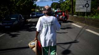 A woman wears a t-shirt bearing a slogan reading 'All against chlordecone' (Chlordecone is a synthetic organic compound which has mainly been used as an agricultural insecticide and fungicide) as she walks near a road block made of burnt vehicles and debris at the cut-off locality of La Boucan in Sainte-Rose in the French Caribbean island of Guadeloupe on November 29, 2021, as France's minister for overseas territories left Guadeloupe at an impasse over ways to end more than a week of violent protests sparked by Covid-19 restrictions. - Unrest in the former colonial outpost began with a protest over compulsory Covid-19 vaccinations for health workers, but quickly ballooned into a broader revolt over living conditions, and spread to next door Martinique. (Photo by Christophe ARCHAMBAULT / AFP)