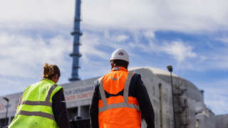 Workers walk past a reactor building at the third-generation European Pressurised Reactor project (EPR) nuclear reactor of Flamanville, Normandy on June 14, 2022. - EDF is to start the Flamanville EPR in 2023 after countless delays and setbacks. (Photo by Sameer Al-DOUMY / AFP)