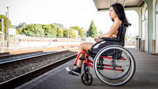 Side view of a lonely teenage girl in a wheelchair on the platform waiting for the train with copy space. Concept of people with reduced mobility.