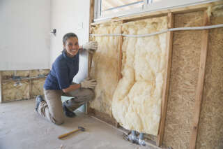 Portrait of a  female worker installing a fiberglass insulation on a wall during wood frame house construction