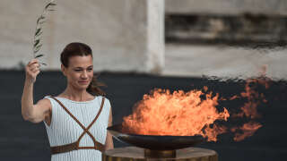 An actress in the role of a priestess stands by the cauldron with the Olympic flame during Olympic flame handover ceremony at The Panathenaic Stadium in Athens, on October 19, 2021. - The flame will be transported by torch relay to Beijing, China, which will host the 2022 Winter Olympics from February 4-20, 2022. (Photo by Louisa GOULIAMAKI / AFP)