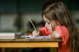 Elementary student writing a dictation in a notebook during a class in the classroom.