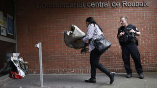 A woman holds a bunch of flowers to be displayed at the entrance of the police station of Roubaix, north of France on May 21, 2023, following a road accident in Villeneuve-d'ascq, causing the death of four people including three policemen belonging to this police station. (Photo by Sameer Al-Doumy / AFP)