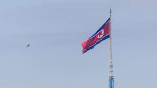 In this picture taken near the truce village of Panmunjom inside the demilitarized zone (DMZ) separating the two Koreas, a bird flies near a North Korean flag fluttering in the wind at the propaganda village of Gijungdong in North Korea on October 4, 2022. North Korea fired a mid-range ballistic missile on October 4, which flew over Japan, Seoul and Tokyo said, a significant escalation as Pyongyang ramps up its record-breaking weapons-testing blitz. (Photo by ANTHONY WALLACE / AFP)