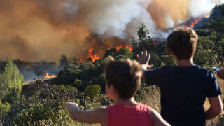 Pedestrians look at a forest fire near Gignac, southern France, on July 26, 2022, as the country endures a dry summer with wildfires destroying numerous forests across France. (Photo by Sylvain THOMAS / AFP)
