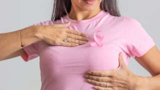 Woman in pink shirt and ribbon holds her breast as a symbol of necessity for prevention checks for women.