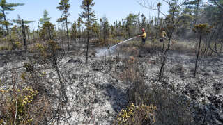 This June 1, 2023, image courtesy of the Nova Scotia Government in Canada, shows firefighters Walter Scott and Zac Simpson spray the ground around Barrington Lake, Shelburne county, Canada. Canada is facing a catastrophic spring wildfire season with massive and powerful blazes out of control in all corners of the country, and thousands more people displaced on June 2, 2023.
