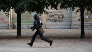 A CRS riot police officer runs past a graffiti reading 
