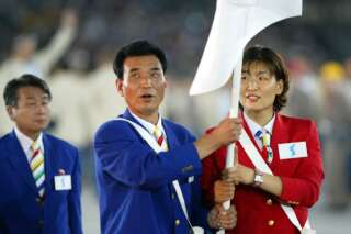 South Korean volleyball player Min Jung Ku (R) and  North Korean Olympic Committe Official Song Ho Kim (C) carry a neutral banner during the opening ceremony of the 2004 Olympic Games at the Olympic Stadium 13 August 2004 in Athens.  In a gesture laden with symbolism, athletes from the Stalinist North and capitalist South entered the Olympic Stadium together under the banner depicting a simple picture of the Korean peninsula.  North and South Korea are divided by the world's last Cold War frontier and remain technically at war as no formal peace treaty was ever signed to end their bloody 1950-53 conflict.    AFP PHOTO / Adrian DENNIS (Photo by ADRIAN DENNIS / AFP)