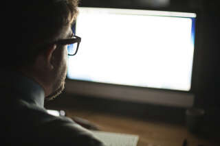 Over the shoulder view of mature man wearing eyeglasses looking at computer monitor.