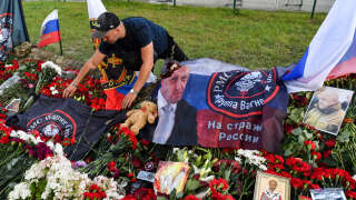 A man arranges a flag bearing the logo of private mercenary group Wagner at a makeshift memorial for Yevgeny Prigozhin in front of the Private Military Company (PMC) Wagner Centre in Saint Petersburg, on August 25, 2023. The plane crash that reportedly killed Yevgeny Prigozhin wiped out the entire top leadership of Russian paramilitary group Wagner but its influence is set to outlive them all both at home and abroad. (Photo by Olga MALTSEVA / AFP)