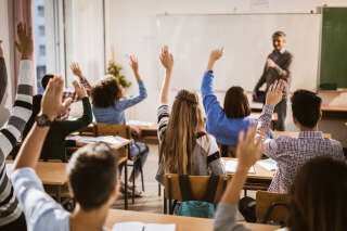 Rear view of large group of students raising their hands to answer the question on a class.